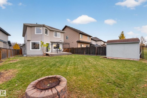 Private backyard featuring a rear wood deck, circular stone fire pit, detached storage shed, and perimeter wood fencing - 7 Bremner, Fort Saskatchewan, AB 