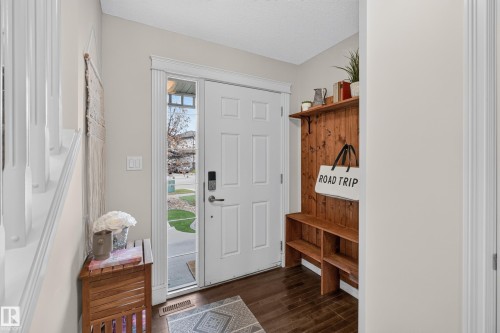Entryway featuring a solid six-panel door with a full-length sidelight, dark wood-finish flooring, and built-in wood wall storage with integrated shelving - 7 Bremner, Fort Saskatchewan, AB 