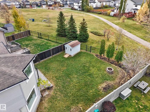 Fenced backyard featuring a wood deck, detached storage shed, stone fire pit, and mature evergreen landscaping - 7 Bremner, Fort Saskatchewan, AB 