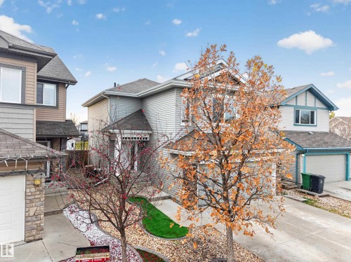 Two-story residence featuring light gray horizontal siding, a concrete driveway, an attached garage, and a covered front entryway with decorative gable detailing - 7 Bremner, Fort Saskatchewan, AB 