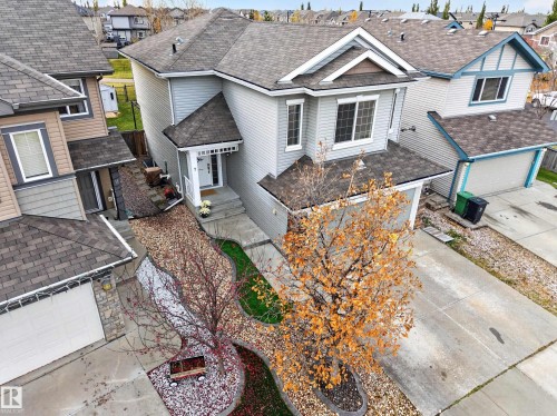 Two-story residence featuring light-toned horizontal siding, a multi-gabled asphalt shingle roof, attached front-entry garage, concrete driveway, and landscaped front yard with decorative stone mulch and concrete curbing - 7 Bremner, Fort Saskatchewan, AB 