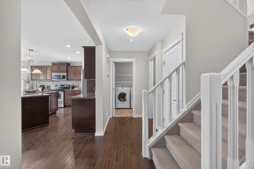 Interior featuring wood-finish flooring, staircase with a white spindle railing, kitchen with dark-finish cabinetry, built-in laundry area, and neutral wall tones - 7 Bremner, Fort Saskatchewan, AB 