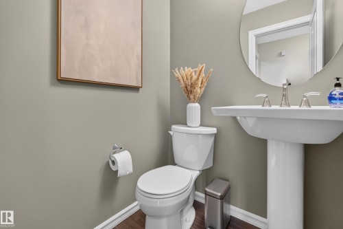 Pedestal sink with a polished chrome widespread faucet, circular wall-mounted mirror, white ceramic toilet, and wood-finish flooring - 7 Bremner, Fort Saskatchewan, AB 