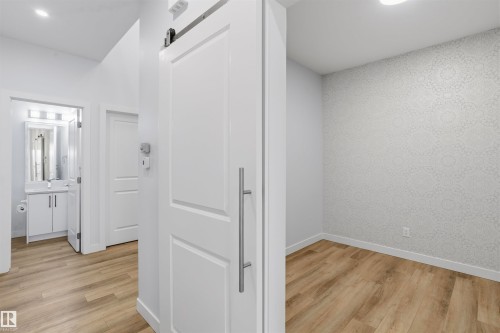 White sliding barn-style door with a vertical stainless steel pull, wood-finish flooring, patterned accent wall, and recessed lighting - 2045 209A St Nw, Edmonton, AB 