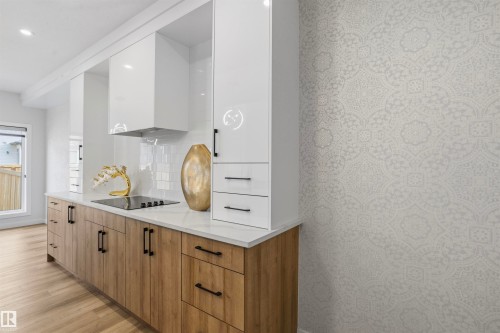 Modern kitchen featuring two-tone cabinetry with gloss white upper units and wood-finish base cabinets, light-toned quartz countertops, a glass tile backsplash, and matte black hardware - 2045 209A St Nw, Edmonton, AB 