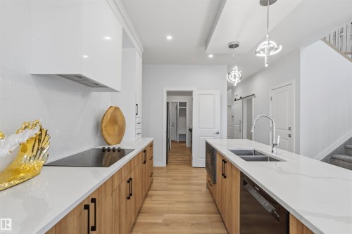 Contemporary kitchen featuring wood-finish cabinetry, white stone countertops, integrated hood vent, dual-basin stainless steel sink with pull-down faucet, and suspended geometric lighting fixtures - 2045 209A St Nw, Edmonton, AB 