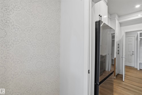 High-gloss white cabinetry, stainless steel refrigerator, patterned wall covering, wood-finish flooring, and recessed ceiling lighting - 2045 209A St Nw, Edmonton, AB 