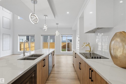 Kitchen featuring quartz countertops, wood-finish cabinetry, a subway tile backsplash, stainless steel under-mount sink, and modern pendant lighting - 2045 209A St Nw, Edmonton, AB 
