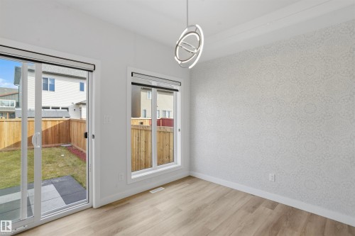 Wood-finish flooring, accent wall with patterned wall covering, modern geometric pendant light fixture, sliding glass door, and backyard access via concrete patio - 2045 209A St Nw, Edmonton, AB 