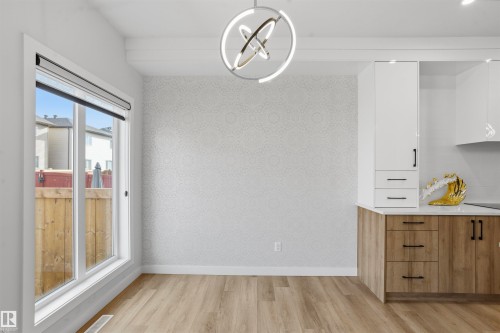 Modern ring-style chandelier, textured wall covering, wood-finish flooring, two-tone cabinetry with matte black hardware, and expansive picture window - 2045 209A St Nw, Edmonton, AB 