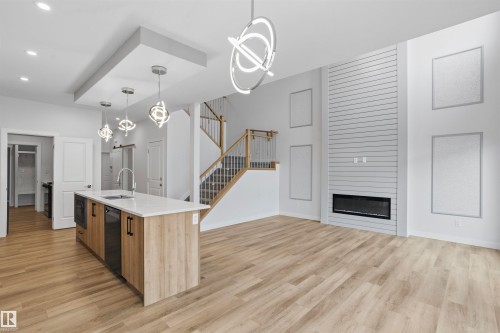Kitchen featuring a center island with quartz countertops, wood-finish cabinetry, linear fireplace with shiplap surround, wood-finish flooring, and modern geometric pendant lighting - 2045 209A St Nw, Edmonton, AB 