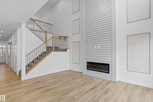 Double-height ceiling, floor-to-ceiling fireplace feature with horizontal slat detailing, built-in electric fireplace, staircase with wood-finish handrail, and light-toned wood-finish flooring - 2045 209A St Nw, Edmonton, AB 