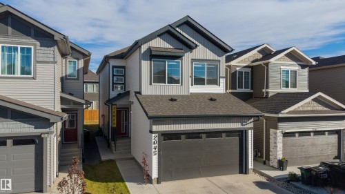 Two-story exterior featuring vertical and horizontal siding, a concrete driveway, an attached garage with glass-paneled detailing, and an asphalt shingle roof - 2045 209A St Nw, Edmonton, AB 