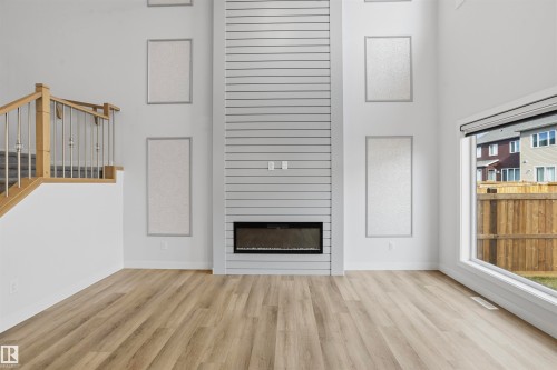 Double-height ceiling, horizontal shiplap fireplace feature wall with integrated electric fireplace, wood-finish flooring, and staircase with wooden handrail and metal balusters - 2045 209A St Nw, Edmonton, AB 