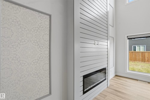 Floor-to-ceiling shiplap fireplace surround with a linear electric insert, wood-finish flooring, high ceilings, and decorative wall paneling - 2045 209A St Nw, Edmonton, AB 