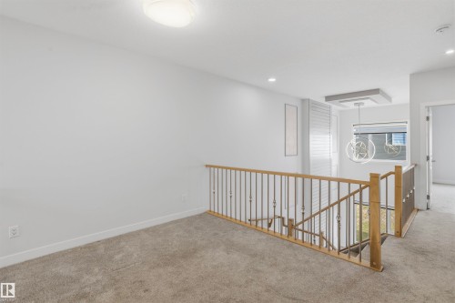 Carpeted flooring, wood-toned handrail with metal balusters, and a modern geometric pendant light fixture - 2045 209A St Nw, Edmonton, AB 