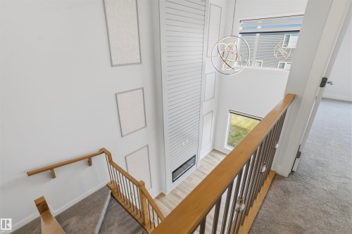 Two-story height ceiling, floor-to-ceiling fireplace surround with horizontal paneling, metal and wood railing, modern orb chandelier, and multi-level window placements - 2045 209A St Nw, Edmonton, AB 
