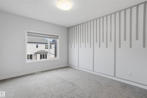 Interior room featuring carpeted flooring, a large window, a ceiling-mounted light fixture, and a decorative vertical slat accent wall - 2045 209A St Nw, Edmonton, AB 
