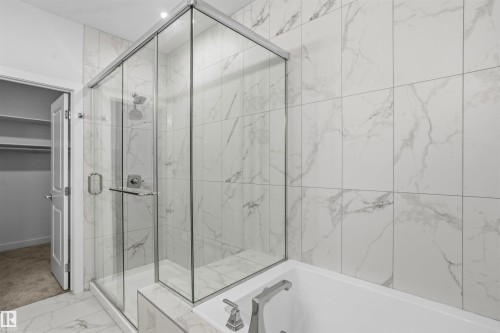 Walk-in shower with a glass enclosure, floor-to-ceiling large-format tile surround, inset soaking tub with metal hardware, and patterned tile flooring - 2045 209A St Nw, Edmonton, AB 