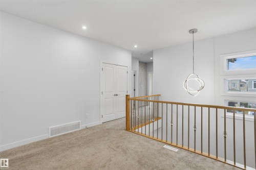 Interior landing featuring a metal spindle railing with wood-finish handrail, contemporary geometric pendant lighting, recessed ceiling lighting, and double-panel doors - 2045 209A St Nw, Edmonton, AB 