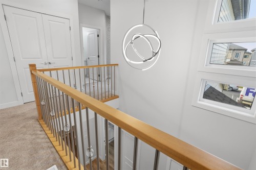 Railing featuring a wood-finish handrail and metal balusters with glass accents, a contemporary orbital-style pendant light fixture, and stacked rectangular windows - 2045 209A St Nw, Edmonton, AB 
