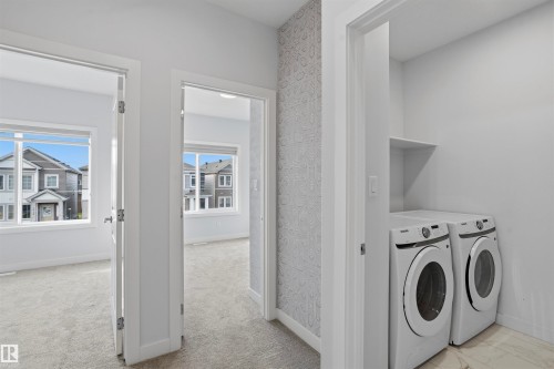 Laundry area featuring built-in shelving, tile flooring, and side-by-side washer and dryer set, accented by a decorative patterned wall - 2045 209A St Nw, Edmonton, AB 