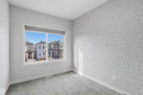 Room interior featuring textured patterned wallpaper, neutral carpeting, and a large window with a built-in roller shade - 2045 209A St Nw, Edmonton, AB 