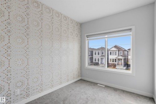 Room featuring an accent wall with geometric patterned wallpaper, neutral carpeting, and a large window with white trim - 2045 209A St Nw, Edmonton, AB 