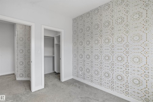 Accent wall featuring geometric patterned wallpaper, neutral carpeting, and a built-in closet system - 2045 209A St Nw, Edmonton, AB 