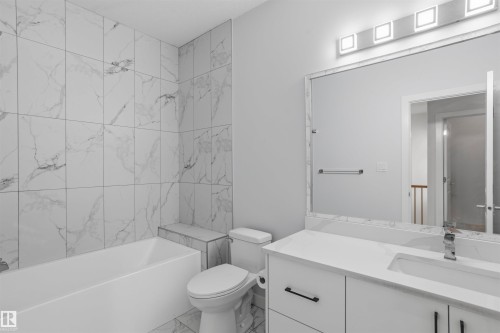 Full-height shower surround with large-format stone-patterned tile, white vanity with integrated basin and quartz countertop, rectangular mirror with tile border, and four-light vanity fixture - 2045 209A St Nw, Edmonton, AB 