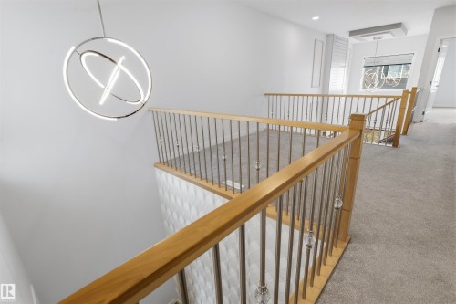 Open landing featuring a wooden handrail, metal balusters with decorative glass accents, dual contemporary ring chandeliers, and neutral wall-to-wall carpeting - 2045 209A St Nw, Edmonton, AB 