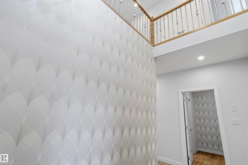Double-height ceiling, geometric-patterned wallpaper, wooden railing with vertical balusters, recessed lighting, and wood-finish flooring - 2045 209A St Nw, Edmonton, AB 