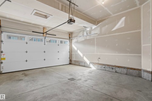Two-car garage featuring a concrete floor, high ceilings, automated door with integrated windows, and drywall finish - 2045 209A St Nw, Edmonton, AB 