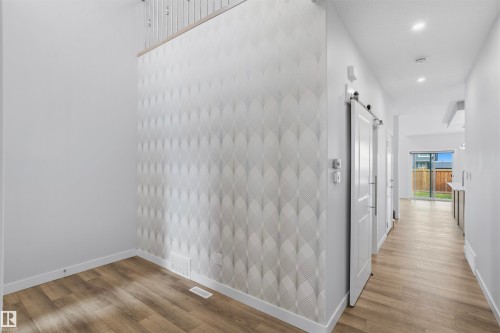 Geometric patterned wallpaper accent wall, wood-finish flooring, recessed lighting, and white sliding barn door with matte black hardware - 2045 209A St Nw, Edmonton, AB 