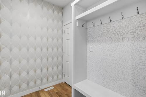 Built-in mudroom bench with overhead shelving and six mounted hooks, featuring patterned accent wallpaper and wood-finish flooring - 2045 209A St Nw, Edmonton, AB 