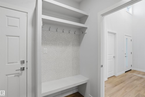 Built-in storage bench featuring patterned tile backsplash, multi-level shelving, chrome finish hooks, and wood-finish flooring - 2045 209A St Nw, Edmonton, AB 