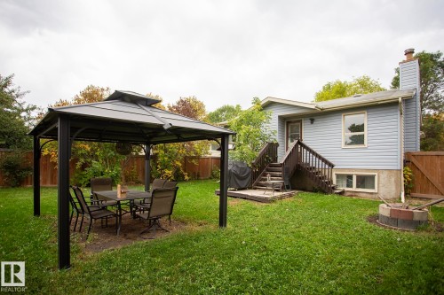 Expansive backyard featuring a metal gazebo, wood privacy fencing, a wood deck, and a brick-finish fire pit - 8 Ash Crescent, St. Albert, AB 
