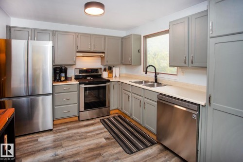 Kitchen featuring wood-finish flooring, gray cabinetry, stainless steel appliances, a double basin sink with a matte black faucet, and light-toned countertops - 8 Ash Crescent, St. Albert, AB 