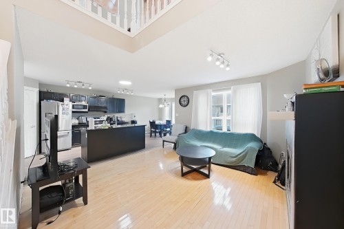 Open-concept living space featuring wood-finish flooring, a kitchen with black cabinetry, a large kitchen island, and a vaulted ceiling with an upper-level overlook - 4 1920 Millwoods Rd E Nw, Edmonton, AB 