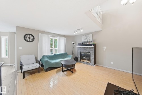 Living area featuring vaulted ceilings, wood-finish flooring, a fireplace with stone-style surround, and an overlook with a white railing - 4 1920 Millwoods Rd E Nw, Edmonton, AB 