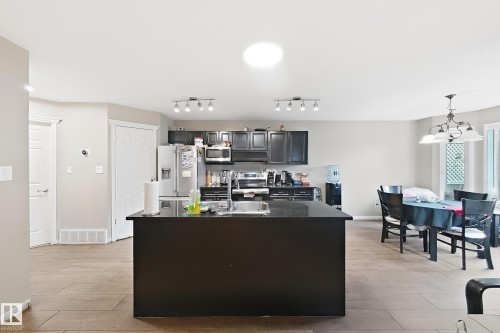 Kitchen featuring a central island with a solid surface countertop, dark-finish cabinetry, stainless steel appliances, tile flooring, and multi-bulb track lighting - 4 1920 Millwoods Rd E Nw, Edmonton, AB 