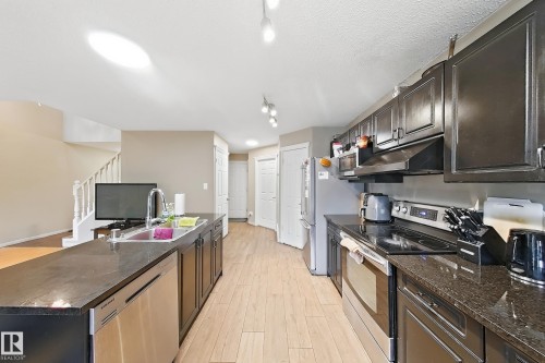 Kitchen featuring dark cabinetry, stone-surface countertops, stainless steel appliances, and wood-finish tile flooring - 4 1920 Millwoods Rd E Nw, Edmonton, AB 