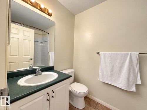 Bathroom featuring white cabinetry, solid-surface countertop with an integrated oval sink, chrome-finish hardware, three-light wall fixture, and tile flooring - 4 1920 Millwoods Rd E Nw, Edmonton, AB 