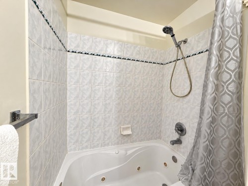 Jetted soaking tub featuring a handheld shower head, integrated wall-mounted soap dish, and patterned ceramic tile surround with decorative accent trim - 4 1920 Millwoods Rd E Nw, Edmonton, AB 
