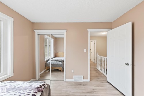 Room featuring wood-finish flooring, mirrored sliding closet doors, multi-panel interior door, and window with white trim - 4 1920 Millwoods Rd E Nw, Edmonton, AB 