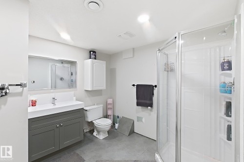 Bathroom featuring a dark-toned vanity cabinet with an integrated white sink, a corner glass-enclosed shower, a wall-mounted medicine cabinet, and tiled flooring - 4 1920 Millwoods Rd E Nw, Edmonton, AB 
