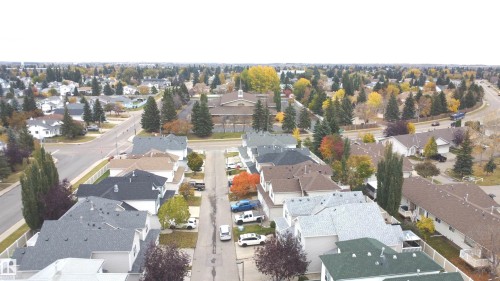 Aerial view of a residential neighborhood featuring multi-level dwellings, mature deciduous and coniferous trees, asphalt roadways, and integrated pedestrian sidewalks - 4 1920 Millwoods Rd E Nw, Edmonton, AB 