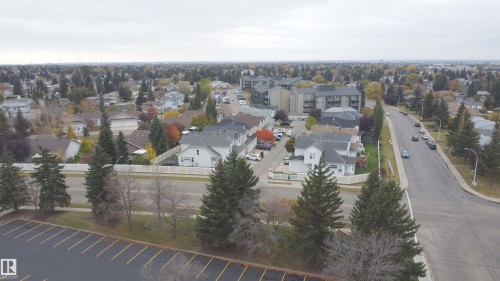 Aerial perspective of a neighborhood setting featuring mature evergreen trees, paved thoroughfares, established residential structures, and asphalt parking areas - 4 1920 Millwoods Rd E Nw, Edmonton, AB 