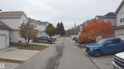 Suburban streetscape featuring light-toned vinyl siding, asphalt shingle roofing, and attached garages with concrete driveways - 4 1920 Millwoods Rd E Nw, Edmonton, AB 