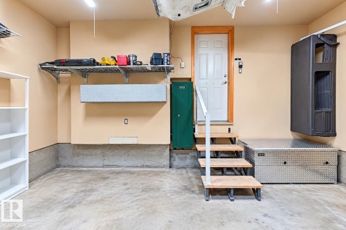 Garage interior featuring concrete flooring, built-in wire shelving, and a metal-treaded staircase with a metal handrail leading to a single-panel service door - 4 1920 Millwoods Rd E Nw, Edmonton, AB 